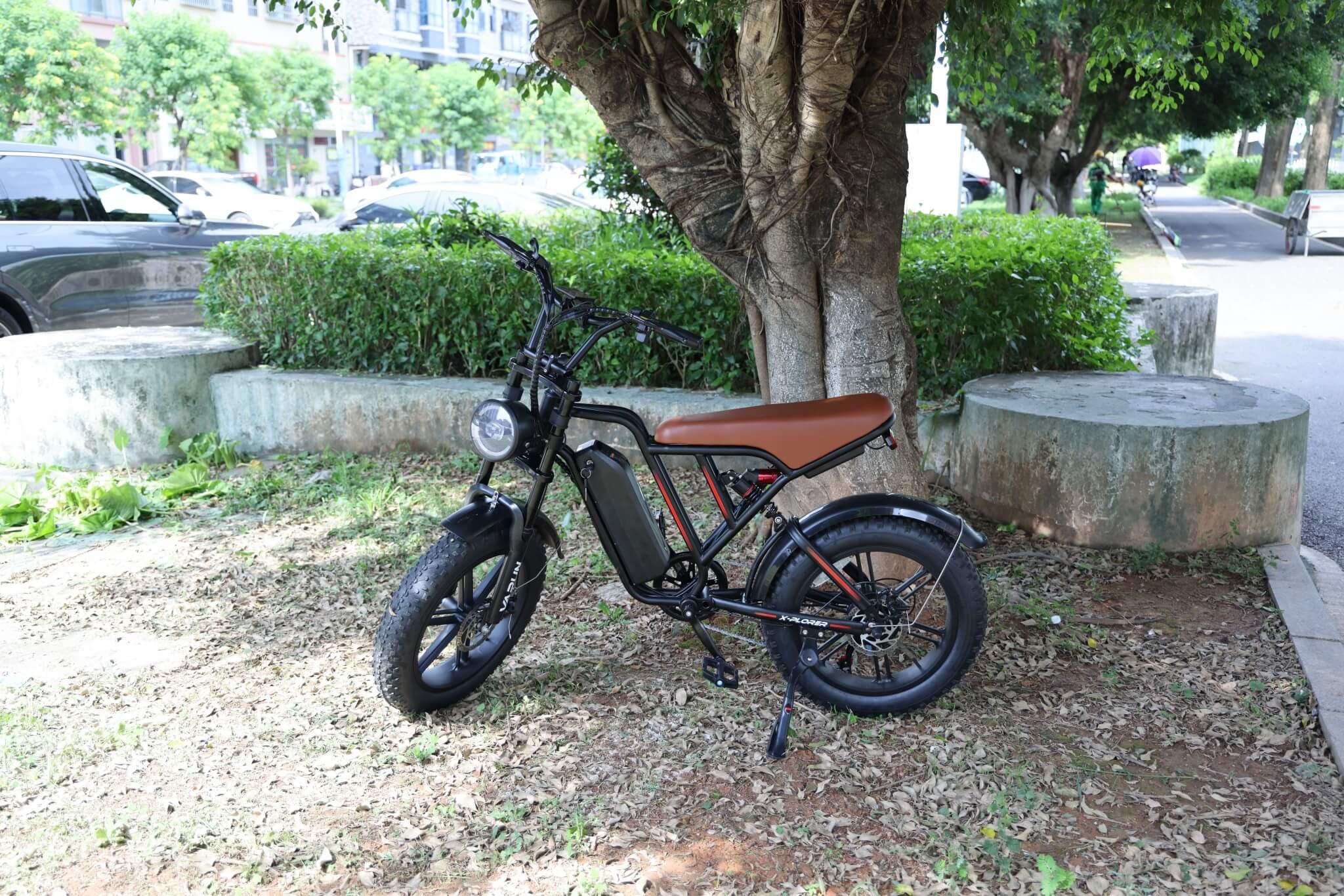 Black electric bike with brown seat parked under tree on grassy patch near street