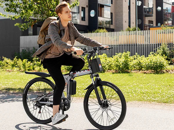 Young man riding a Varun electric bike on a sunny urban street with modern buildings and greenery