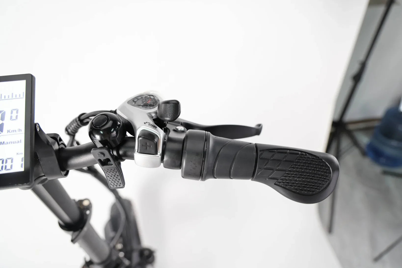 Close-up of a black bicycle handlebar with ergonomic grip, brake lever, bell, and digital speedometer