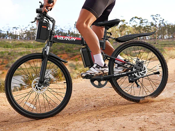 Person riding a black and red Varun mountain electric bike on a dirt path outdoors