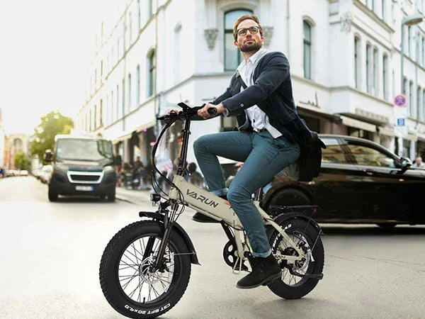 Young man in smart casual outfit riding Varun electric bike on city street with buildings and cars