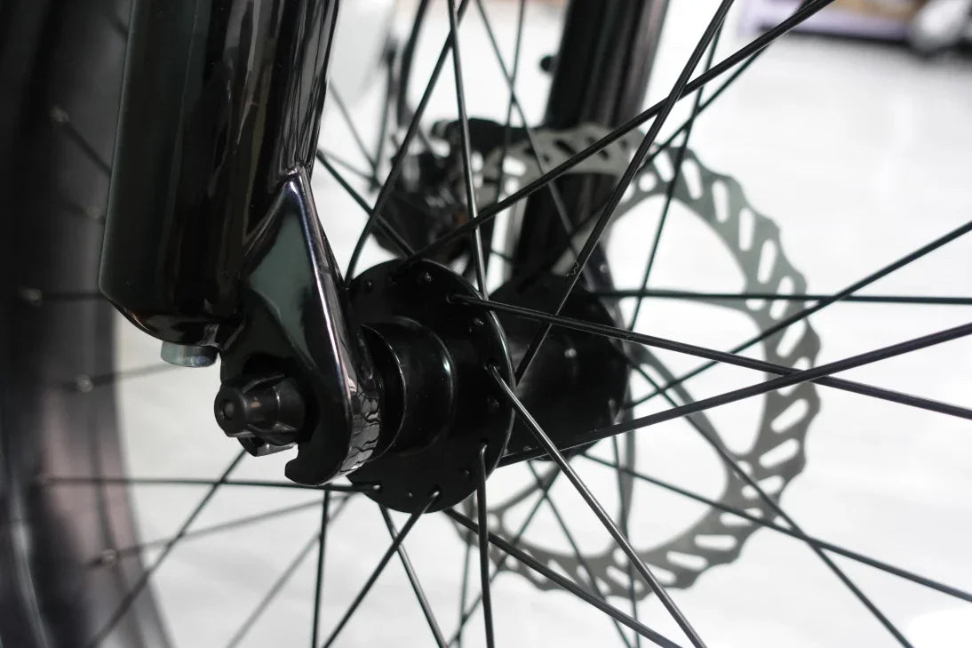 Close-up of black bicycle front wheel hub and disc brake rotor with thin spokes