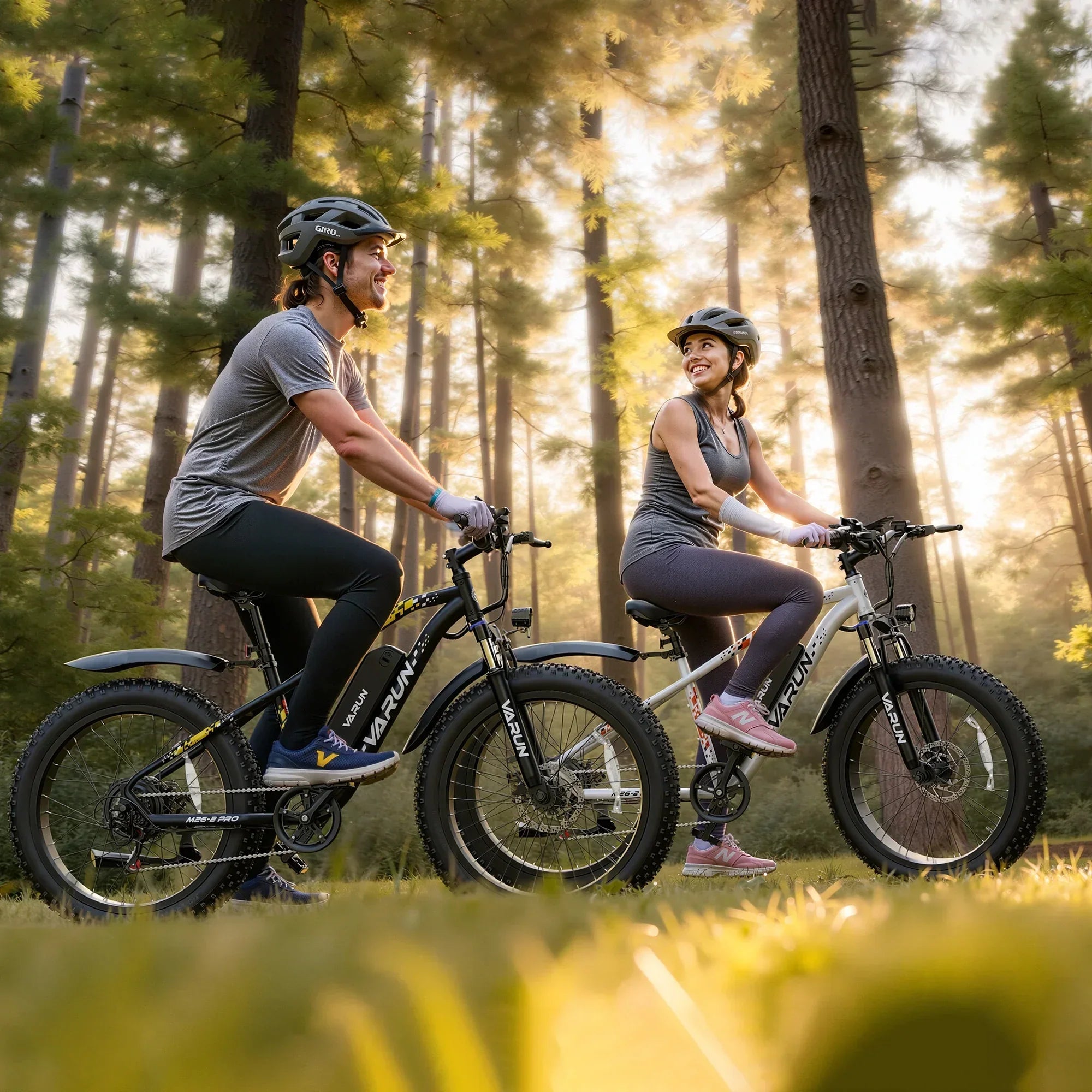 Man and woman wearing helmets riding Varun mountain bikes in a sunlit forest