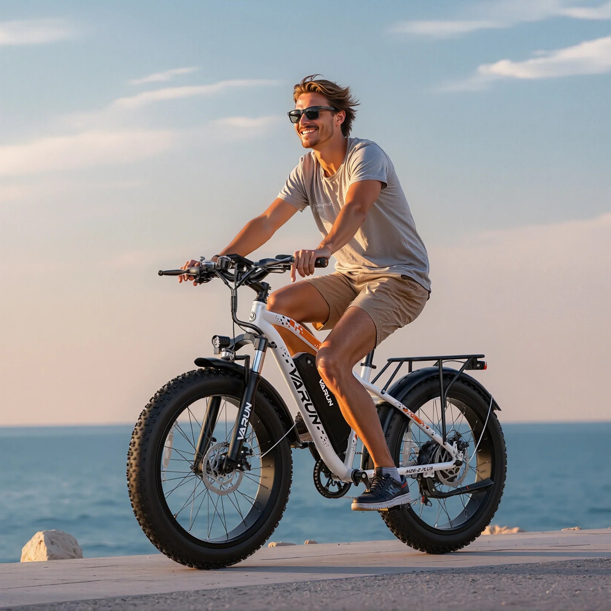Smiling man wearing sunglasses riding a white Varun electric fat tire bike by the sea at sunset
