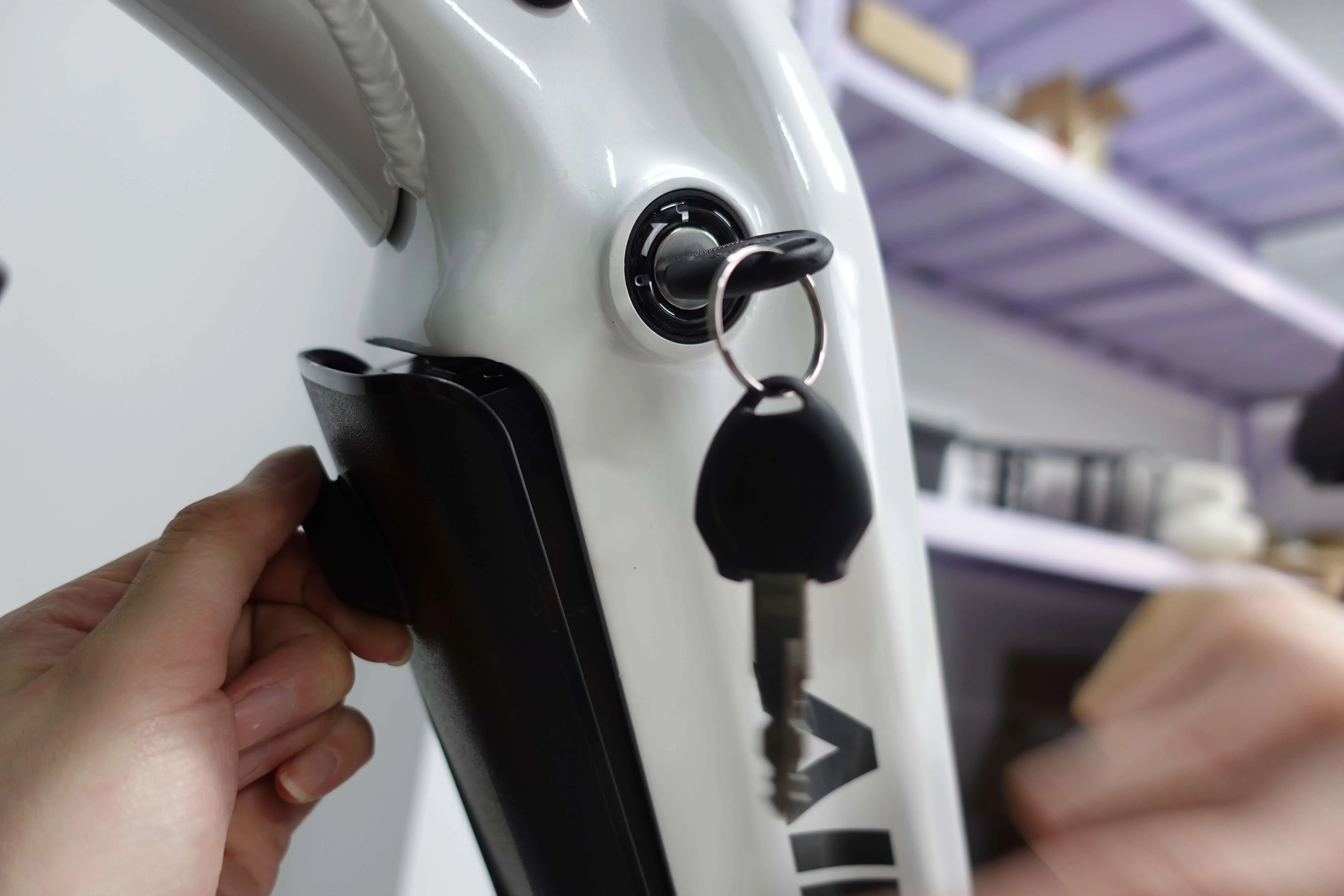 Hand inserting key into white electric bike battery lock with black battery pack in background