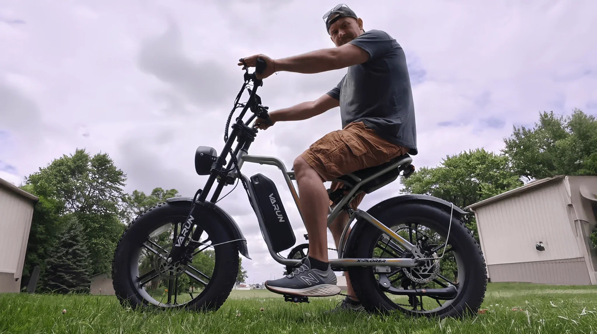 Man wearing cap, t-shirt, and shorts riding a Varun X-Plorer electric bike on grass