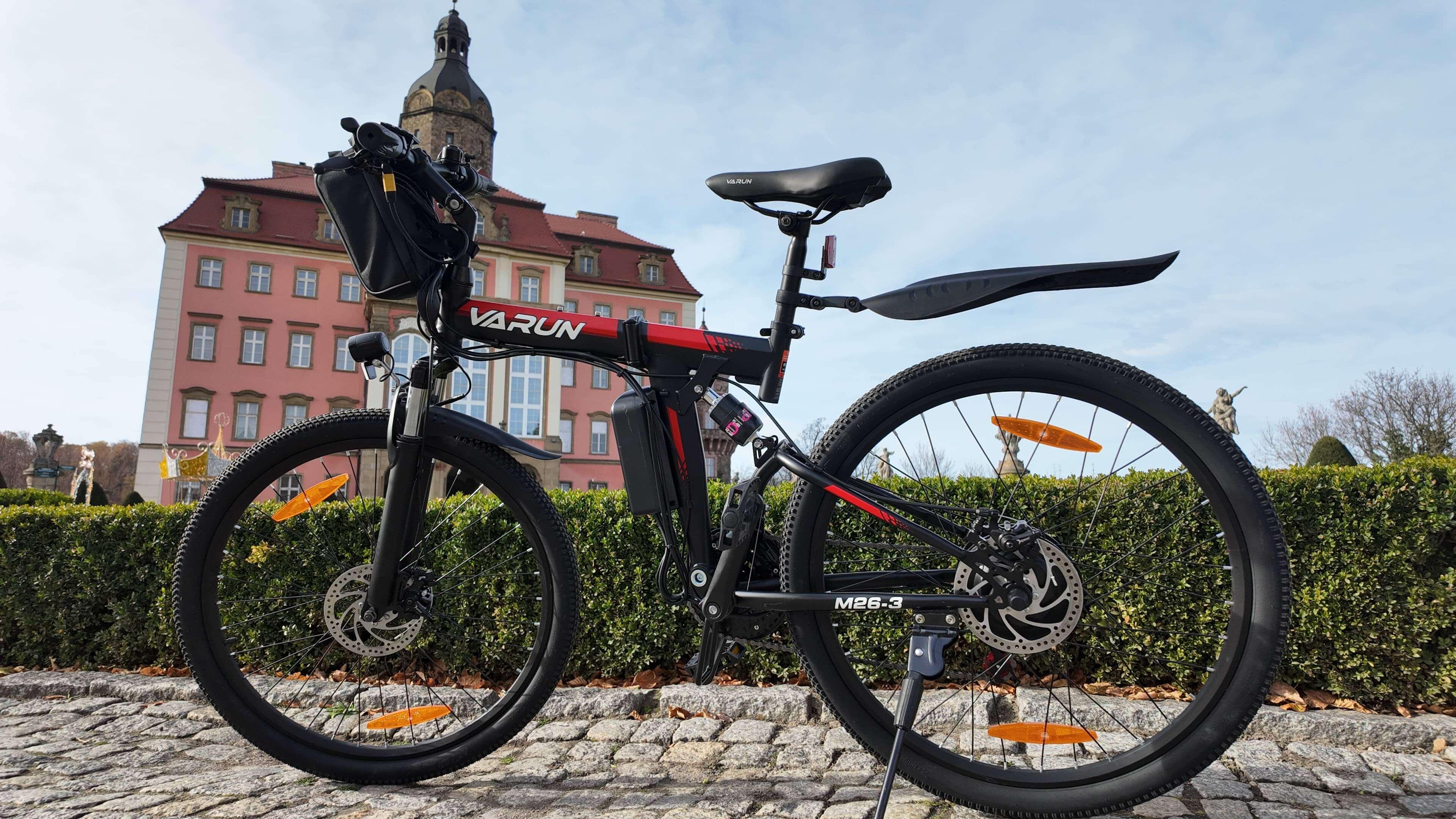 Black and red Varun M26-3 electric mountain bike parked on cobblestones with historic building in background
