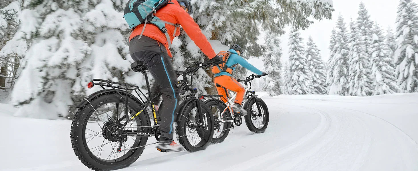 Two cyclists wearing winter gear riding fat tire bikes on a snowy forest trail