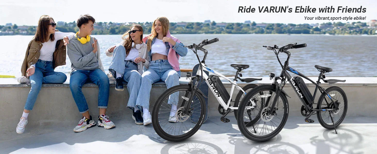 Four friends sitting by the waterfront with two VARUN sport-style electric bikes nearby on a sunny day