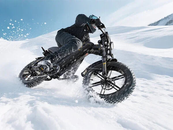 Person riding black electric fat-tire bike on snow-covered terrain under blue sky