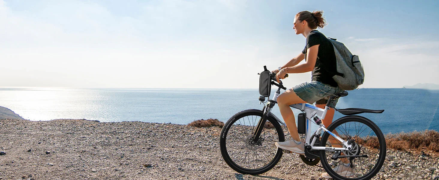 Woman riding white electric bike on rocky trail overlooking ocean under clear sky