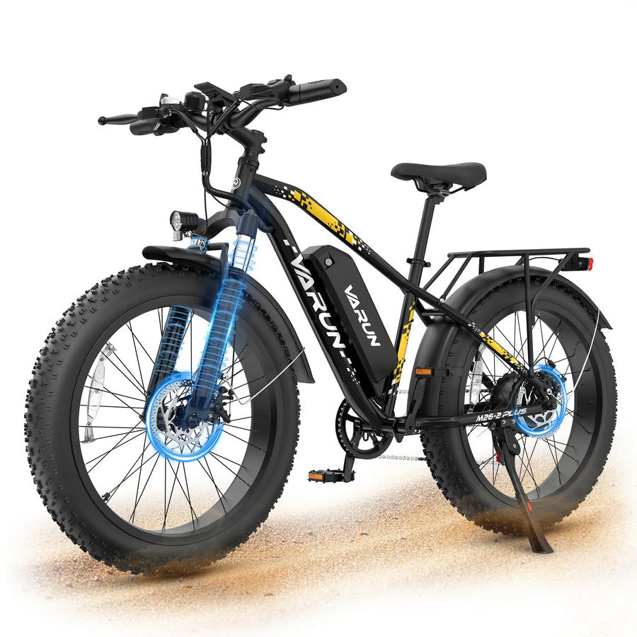 Black and yellow Varun electric fat tire bike with front suspension, rear rack, and disc brakes on sandy ground