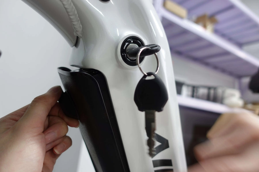 Hand inserting key into white electric bike battery lock with black battery pack in background